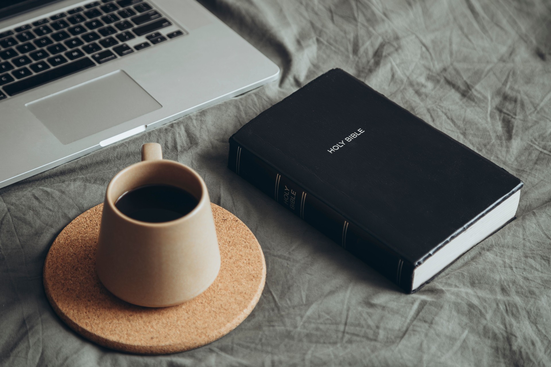 Cup of coffee, Bible book and laptop on gray bed in bedroom, cozy mood.